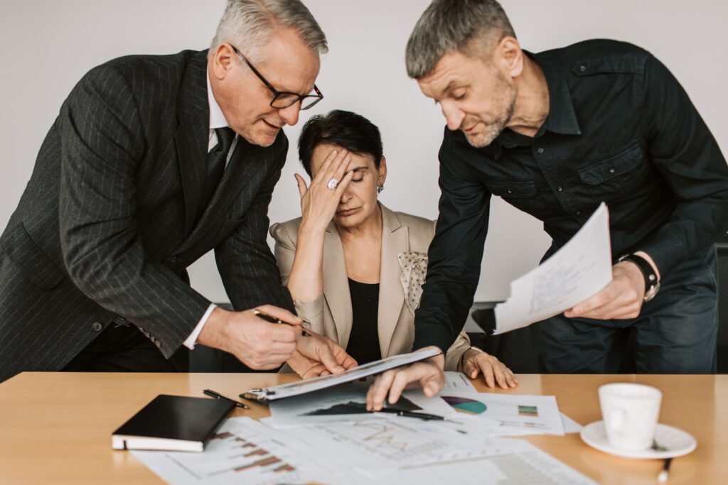 woman at desk head in hands experiencing decision fatigue with two people asking her questions