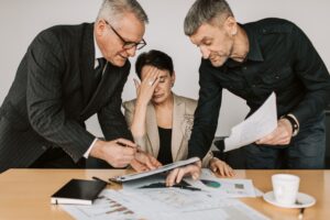 woman at desk head in hands experiencing decision fatigue with two people asking her questions